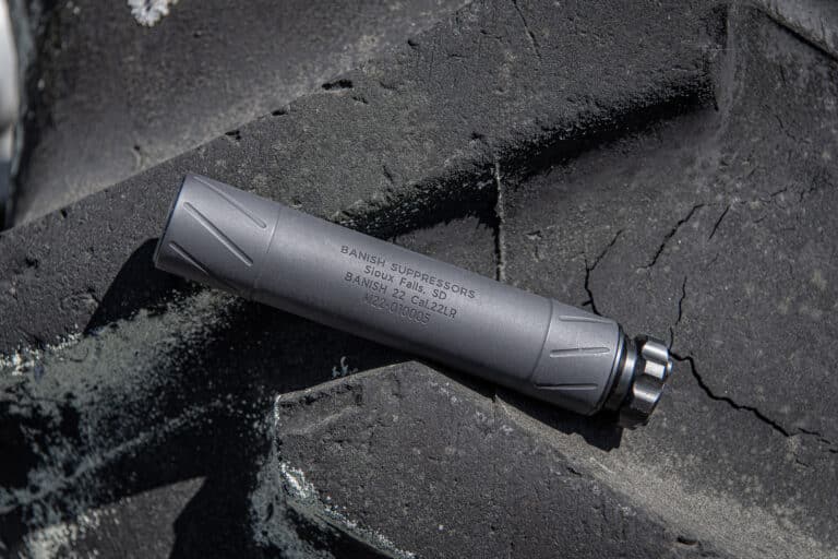 Close-up of a gray tactical pen resting on a dark, rough rock surface; engraving partially visible on the pen's body.