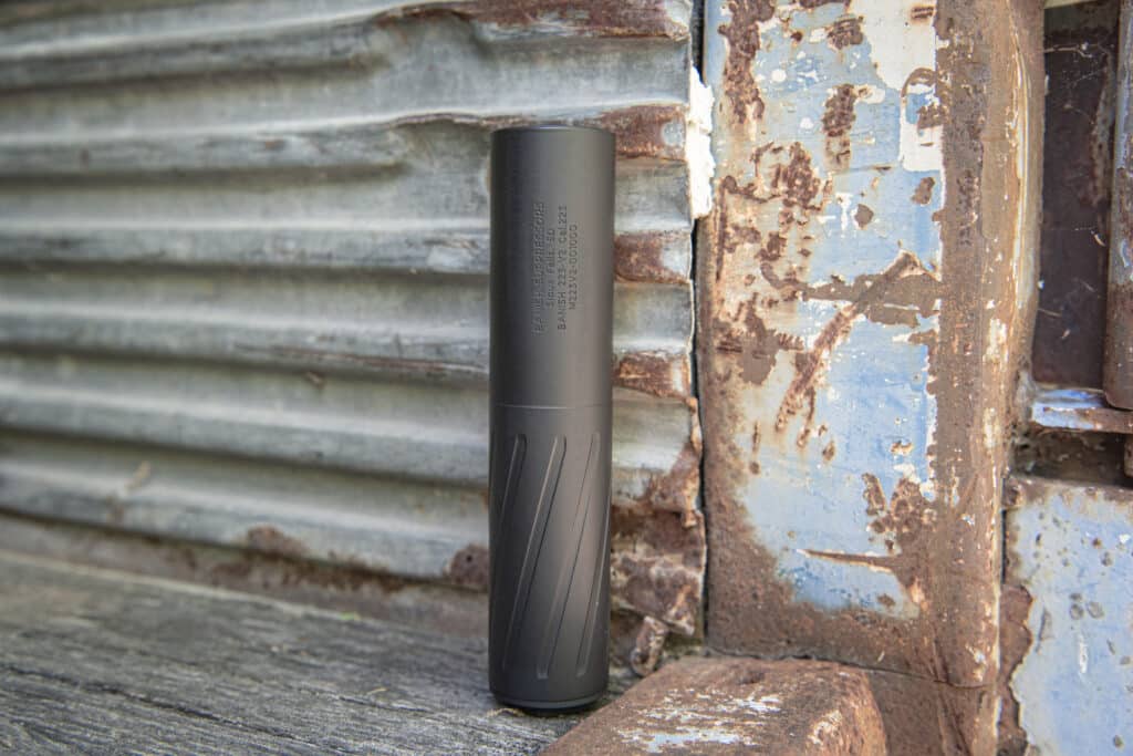 Matte black vape mod standing upright against a corrugated metal wall with peeling rust and blue paint.