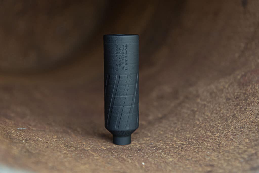 Close-up of the top end of a black cylindrical tool with a textured grip, standing on a rust-colored surface.
