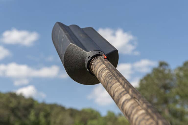 Close-up of a black canoe paddle blade attached to a wooden shaft against a blue sky.