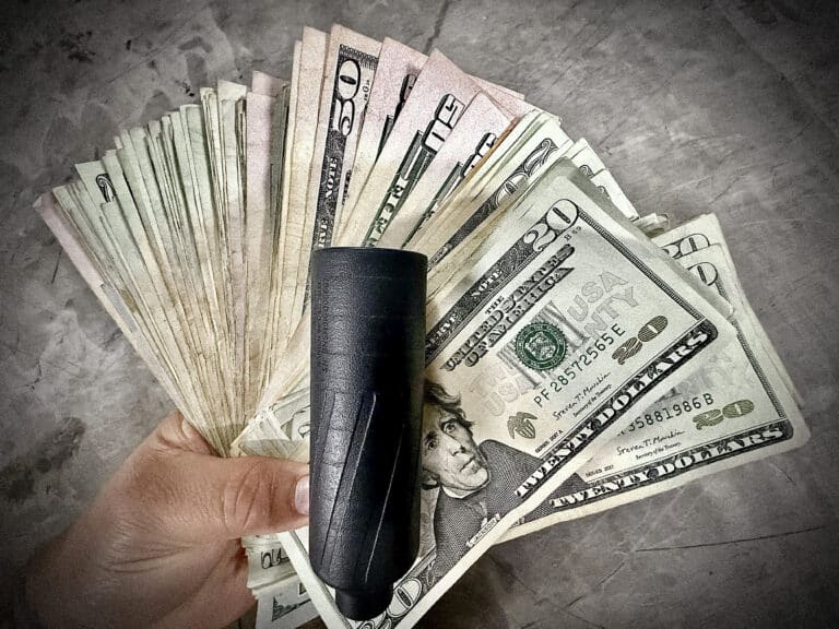 Hand holding a fan of assorted US dollar bills with a black wallet resting on top.