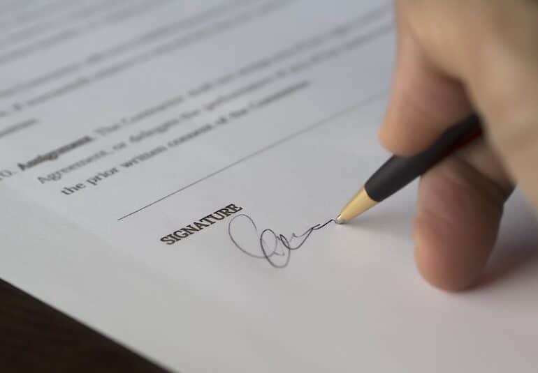 Close-up of a hand signing a document at the signature line with a pen