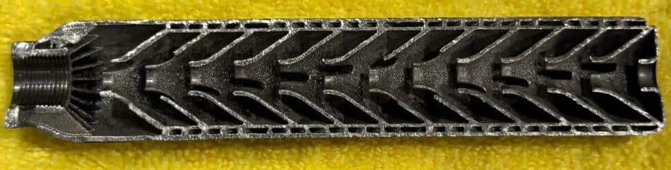 guns americ digest suppressor construction - PopularSuppressors Long rectangular metal lattice bar with chevron-shaped cutouts on a yellow background. Left end shows a threaded section and ridges.