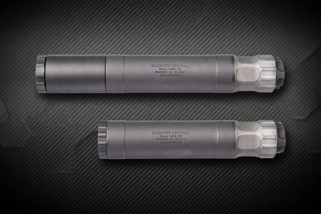 Two matte gray firearm silencers laid parallel on a dark carbon-fiber background, one near the top and one below it.
