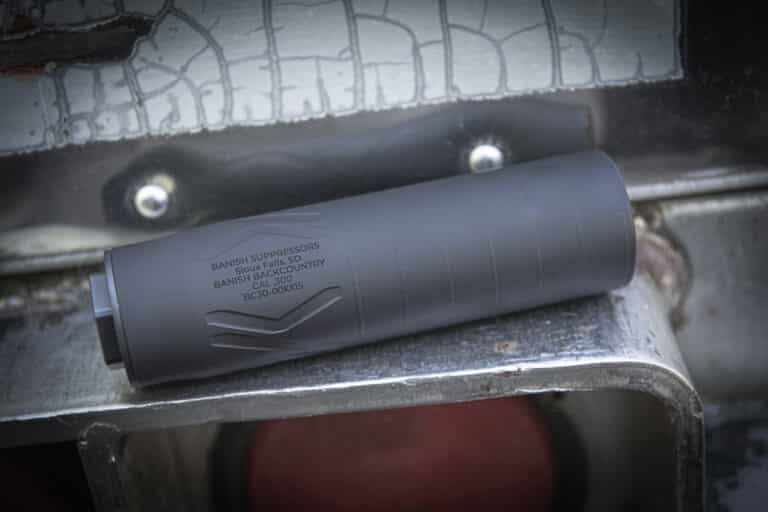 Close-up of a gray firearm suppressor resting on a metal work surface, with engraved branding visible.