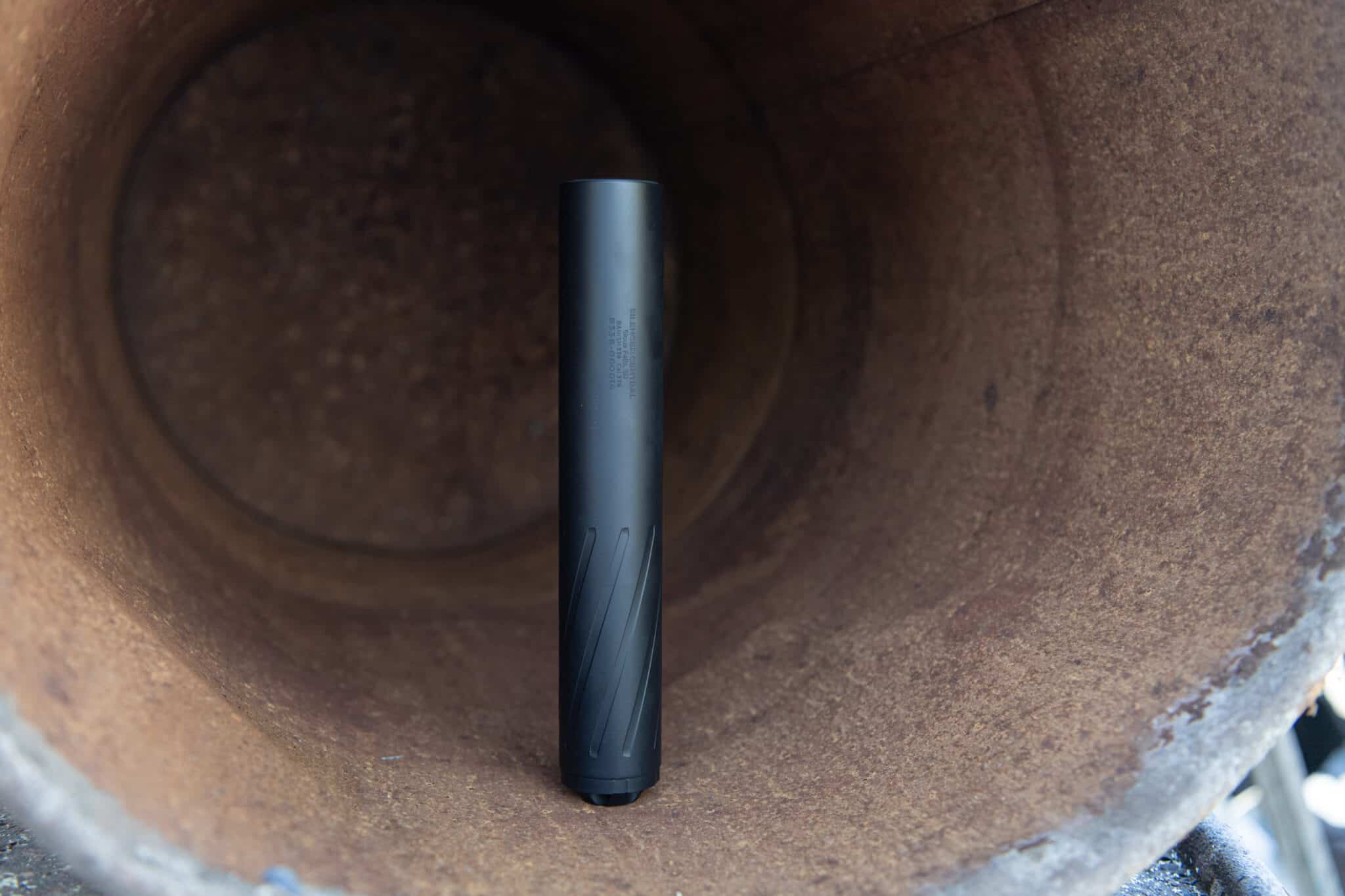 Black cylindrical rod inserted vertically into a brown, rusted pipe interior; some small engravings are visible on the rod's surface.