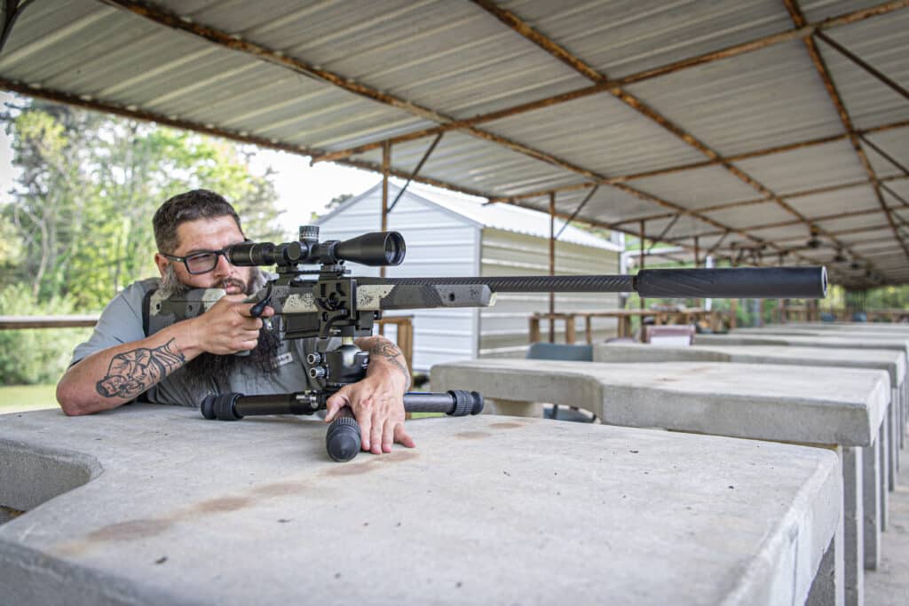 A long-range precision rifle fitted with the BANISH 338 titanium .338-caliber suppressor, sighted-in from a prone position on an outdoor concrete shooting bench.