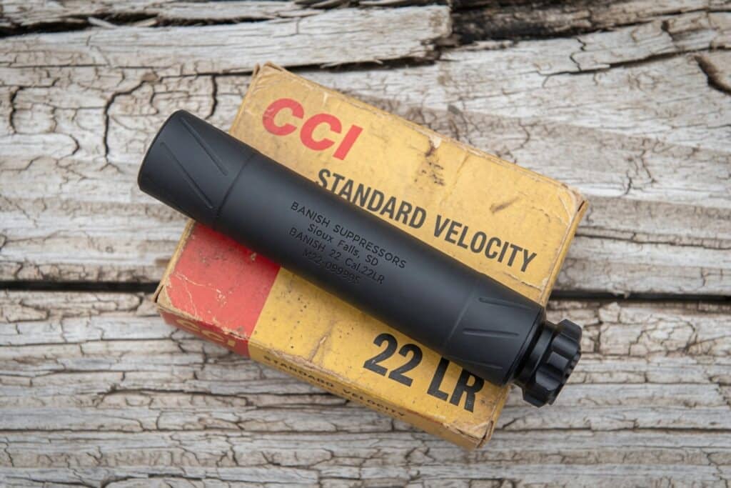 Black .22 LR suppressor resting on a yellow CCI Standard Velocity box on a weathered wooden surface, box text visible.