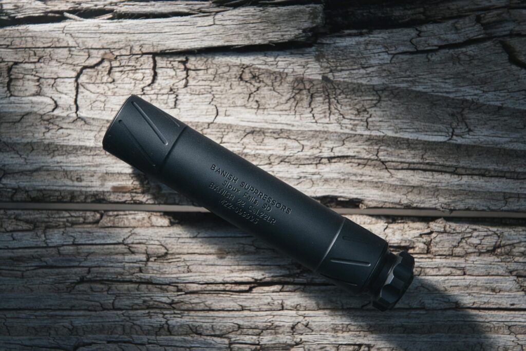 Matte black firearm suppressor lying diagonally on weathered cracked wood, with engraved text along the body.