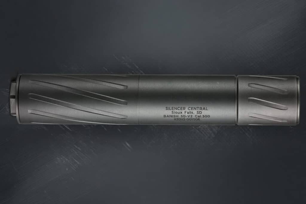 Long gray firearm suppressor lying horizontally on a dark surface, with branding text along the body (SILENCER CENTRAL).