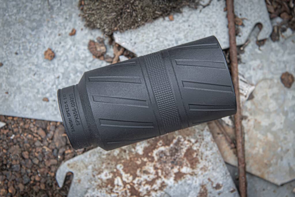 A black handgun/ rifle magazine lying on a rusty metal surface with gravel and debris around it.