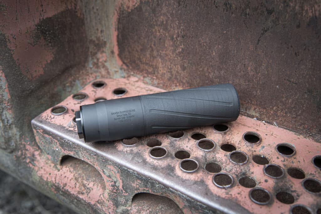 Black firearm suppressor resting on a rusted perforated metal surface, close-up detail.