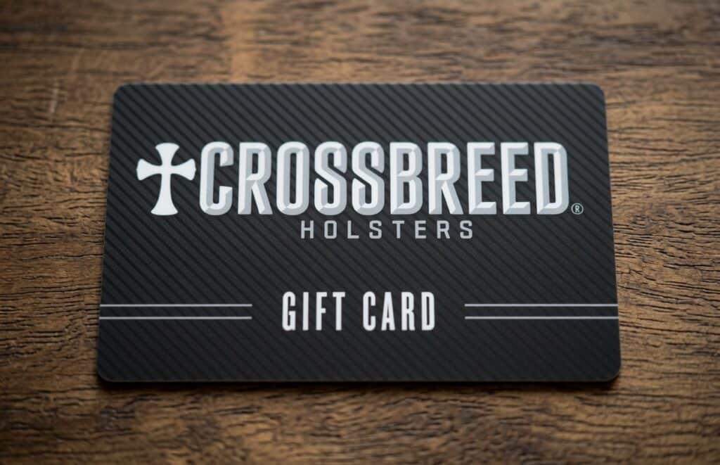 CrossBreed Holsters gift card on a dark striped card resting on a wooden surface, displaying the brand name and 'Gift Card' text.