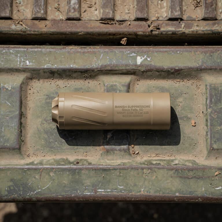 Tan firearm suppressor lying on a dirty, green metal surface. (Informative image)