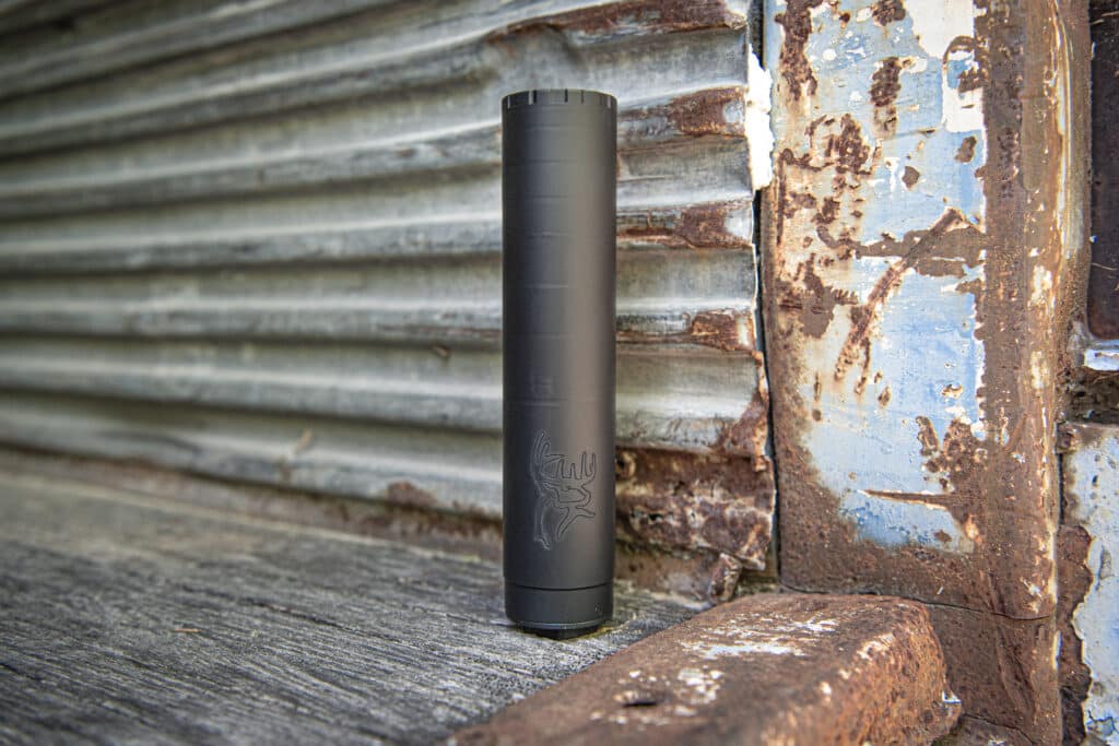Black cylindrical vape device standing upright on a weathered wooden surface with a rusted, peeling metal backdrop behind it.
