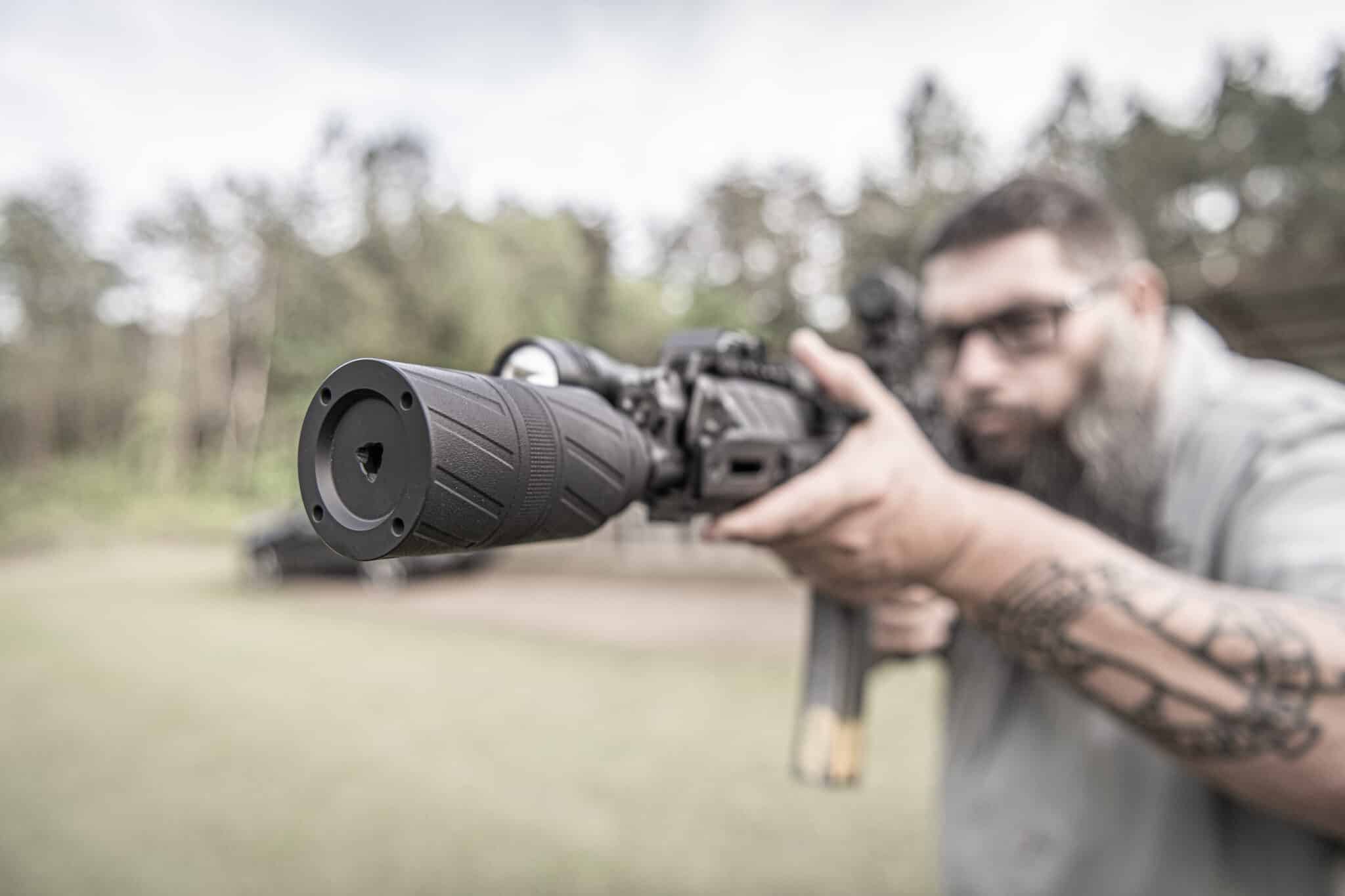 Shooter aiming a scoped rifle with a short suppressor on the muzzle