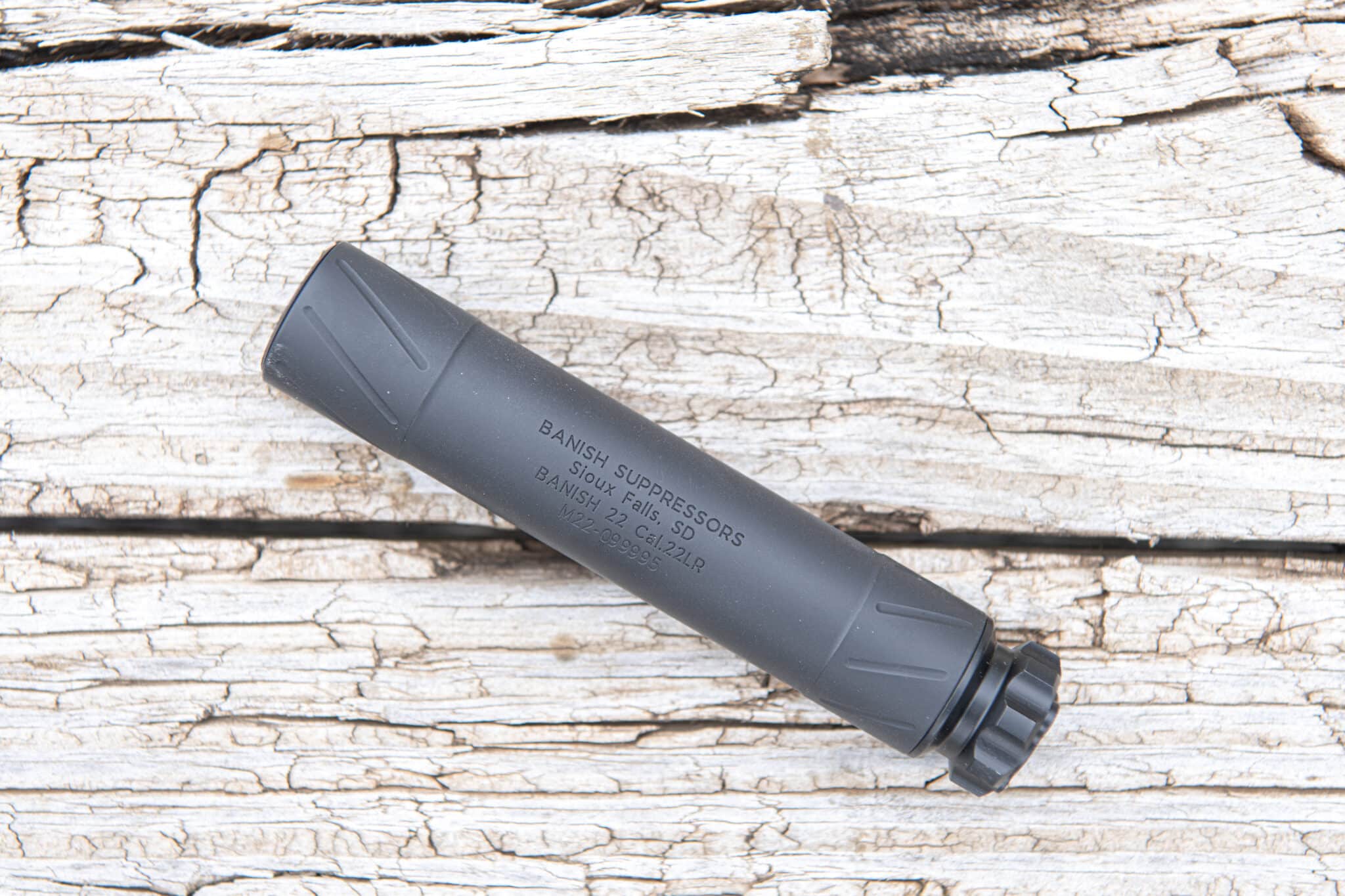 Gray firearm suppressor resting on weathered wooden boards, diagonally across the frame.