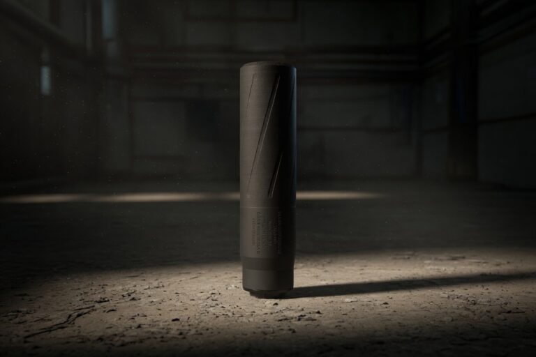 A tall black cylindrical device stands upright on a dusty warehouse floor, lit by a single spotlight in a dark, industrial space.