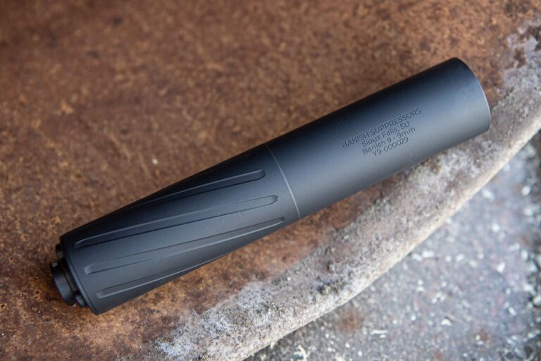 Black suppressor resting on a rusted surface, with engraved text including 'BANISH SUPPRESSORS' and location details Sioux Falls, SD