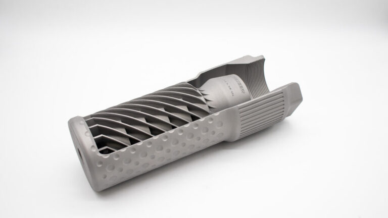 SIlencer-MK-1024x576 - PopularSuppressors Gray 3D-printed cylindrical part with an internal spiral lattice and perforated outer shell.