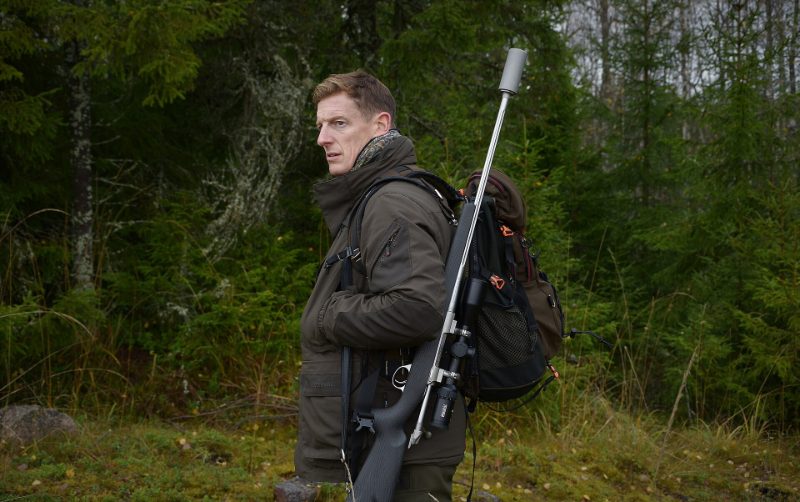 Hunter carrying a bolt-action rifle with a mounted suppressor on a fall hunt